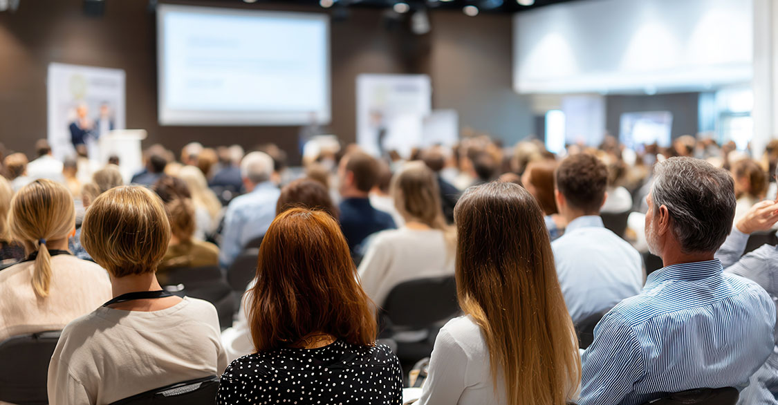 Professionals networking, listening intently to keynote speaker sharing knowledge in crowded conference hall with collaborative energy